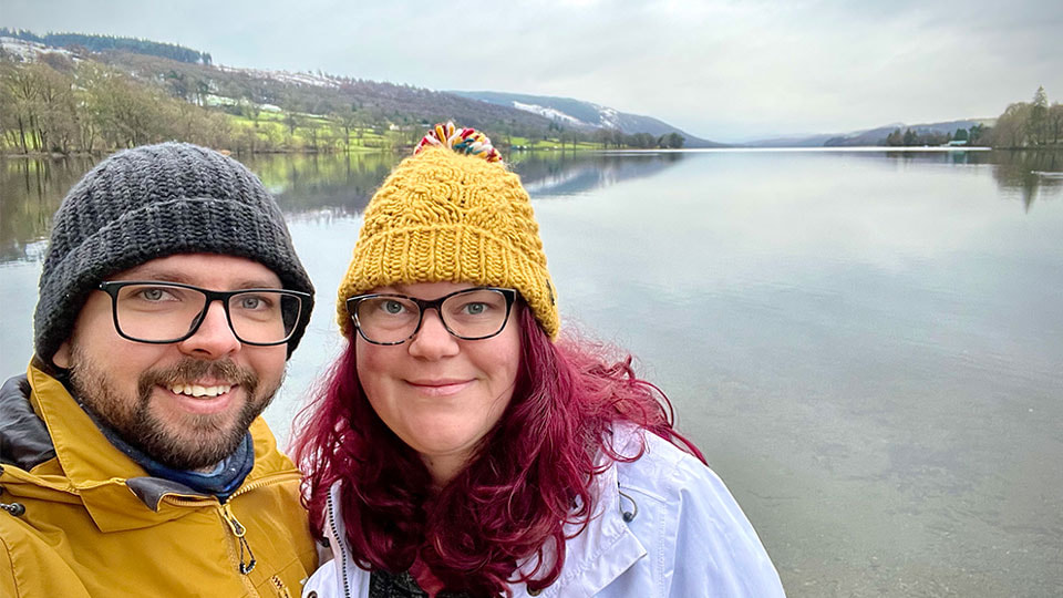 Martin and April infront of Coniston water. Both are wearing wooly hats as you can see some snow on the hills in the background.