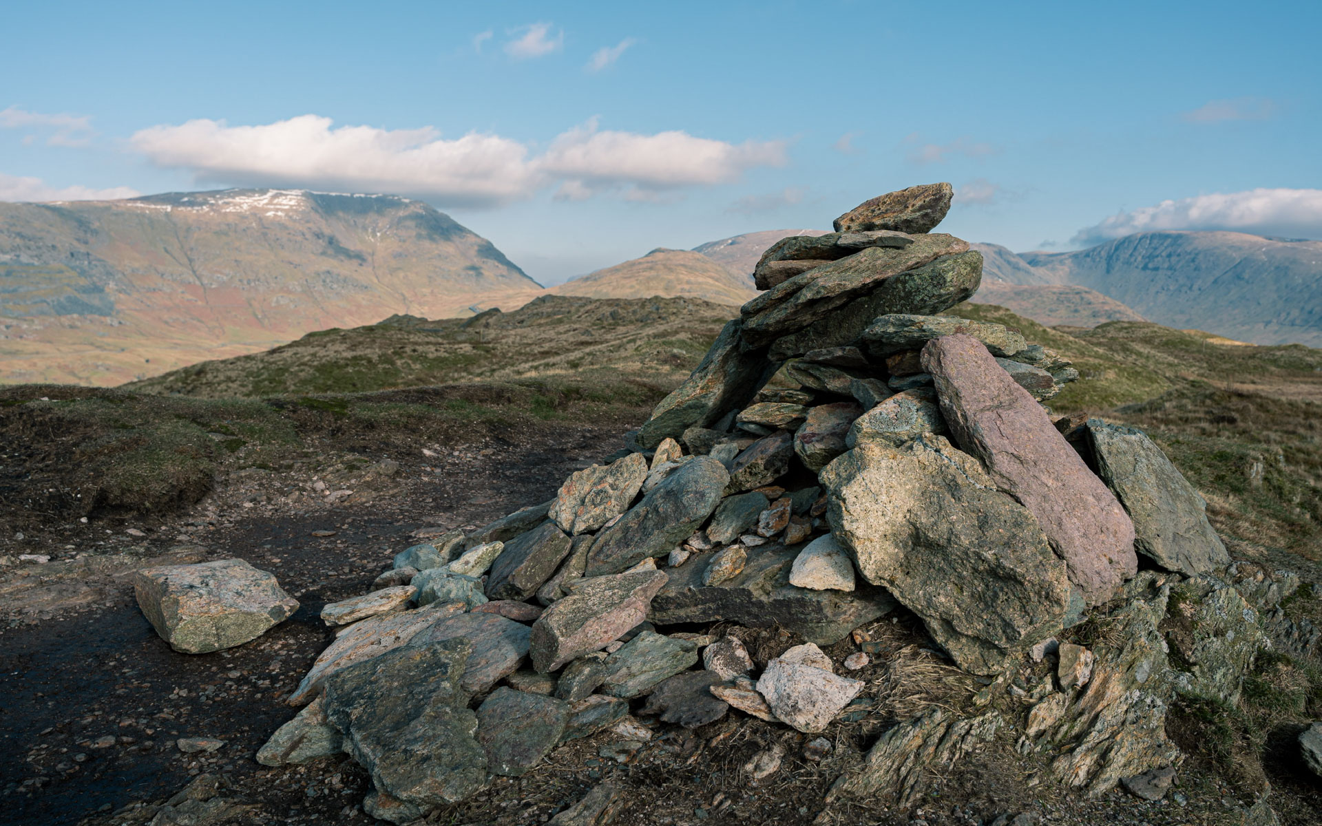 The stone cairn at the top of Wansfell. In the background you can see Red Screes with a little snow on top. The sky is clear blue with just a few white clouds.